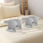 Four white plastic bed sheet fastener clips arranged on a beige bed, and there is a softly blurred bedroom background.