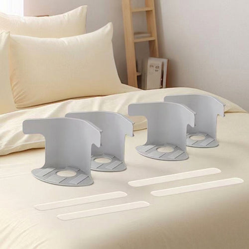 Four white plastic bed sheet fastener clips arranged on a beige bed, and there is a softly blurred bedroom background.