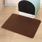Brown mat with honeycomb pattern in front of a light blue litter box on a wooden floor.