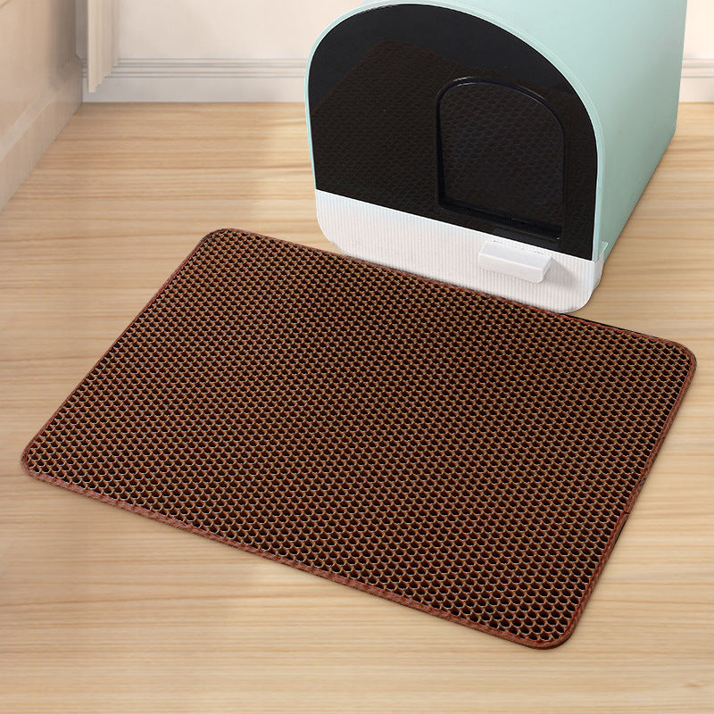 Brown mat with honeycomb pattern in front of a light blue litter box on a wooden floor.